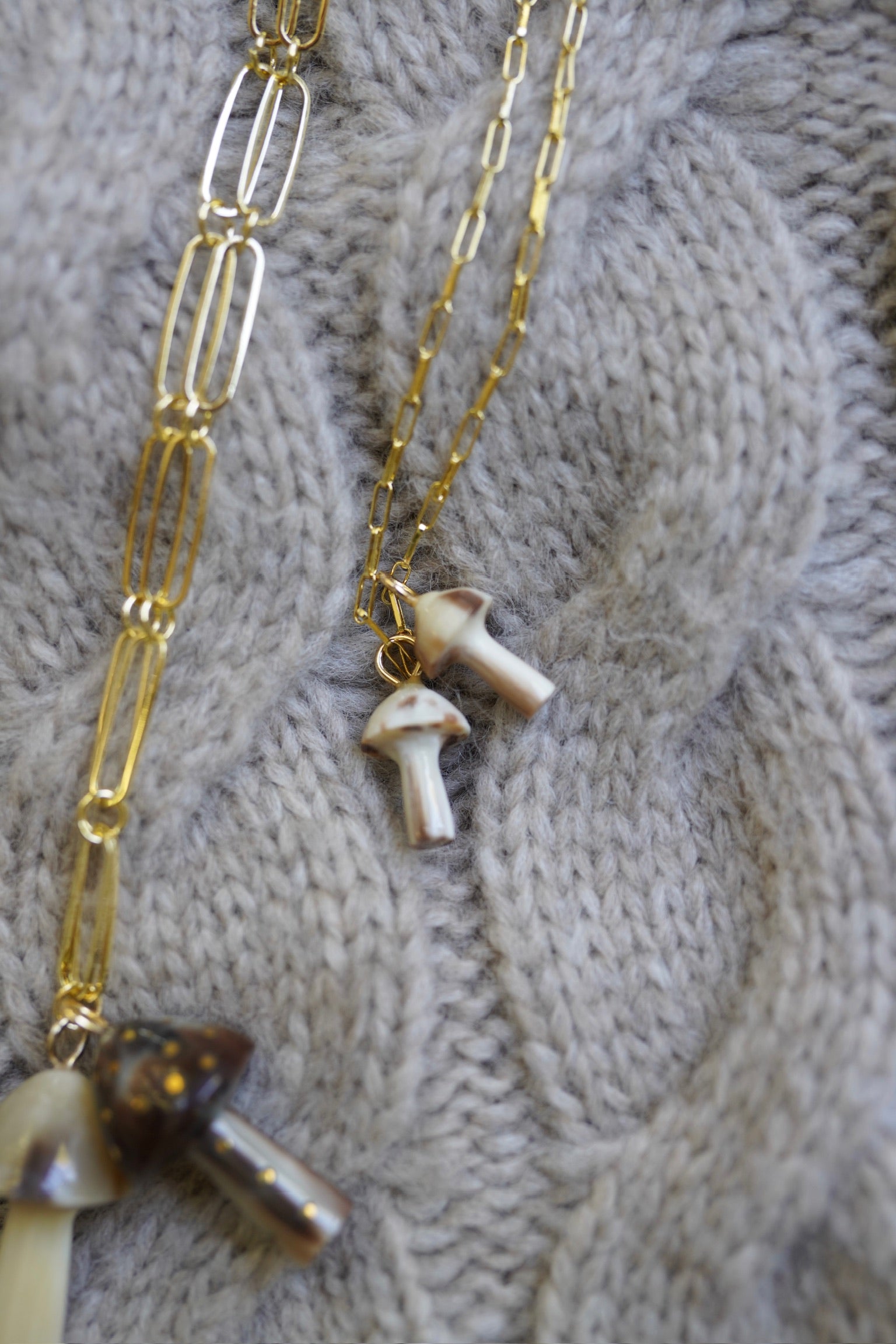 Paper clip gold chain necklace with mushroom charms on a textured gray background