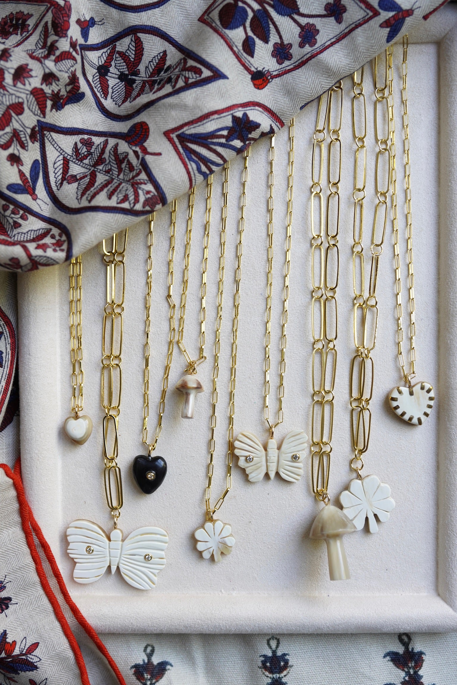 Gold necklaces with various pendants on a white tray, with a patterned fabric in the background.