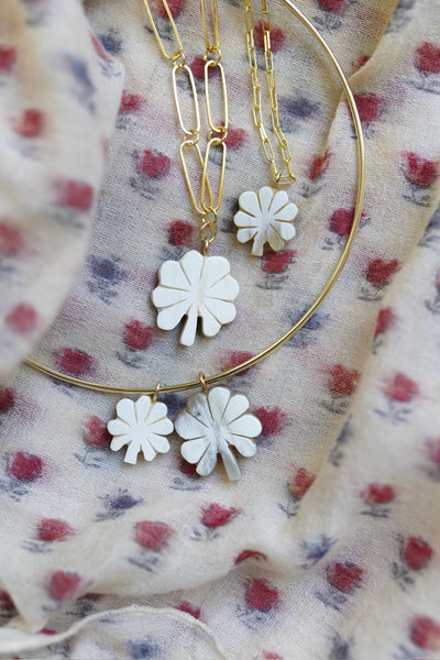 Gold hoop earrings with white floral designs on a floral fabric background