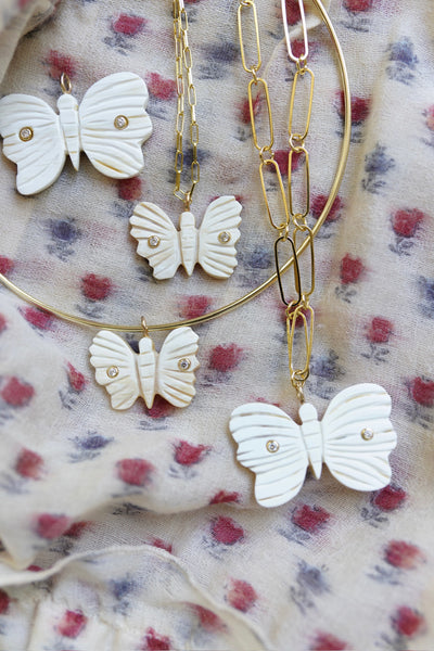 Butterfly-shaped pendants on gold chains against a floral fabric background