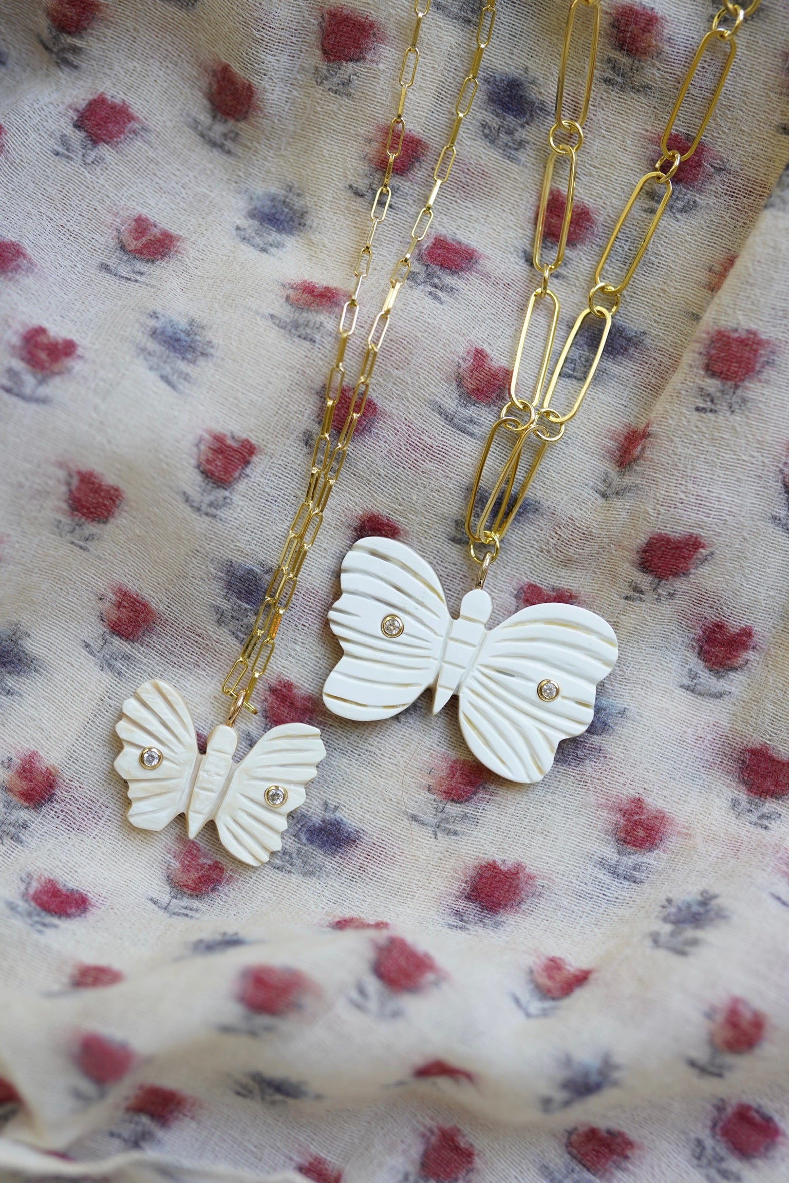 Butterfly-shaped charm pendants on gold chains against a floral fabric background