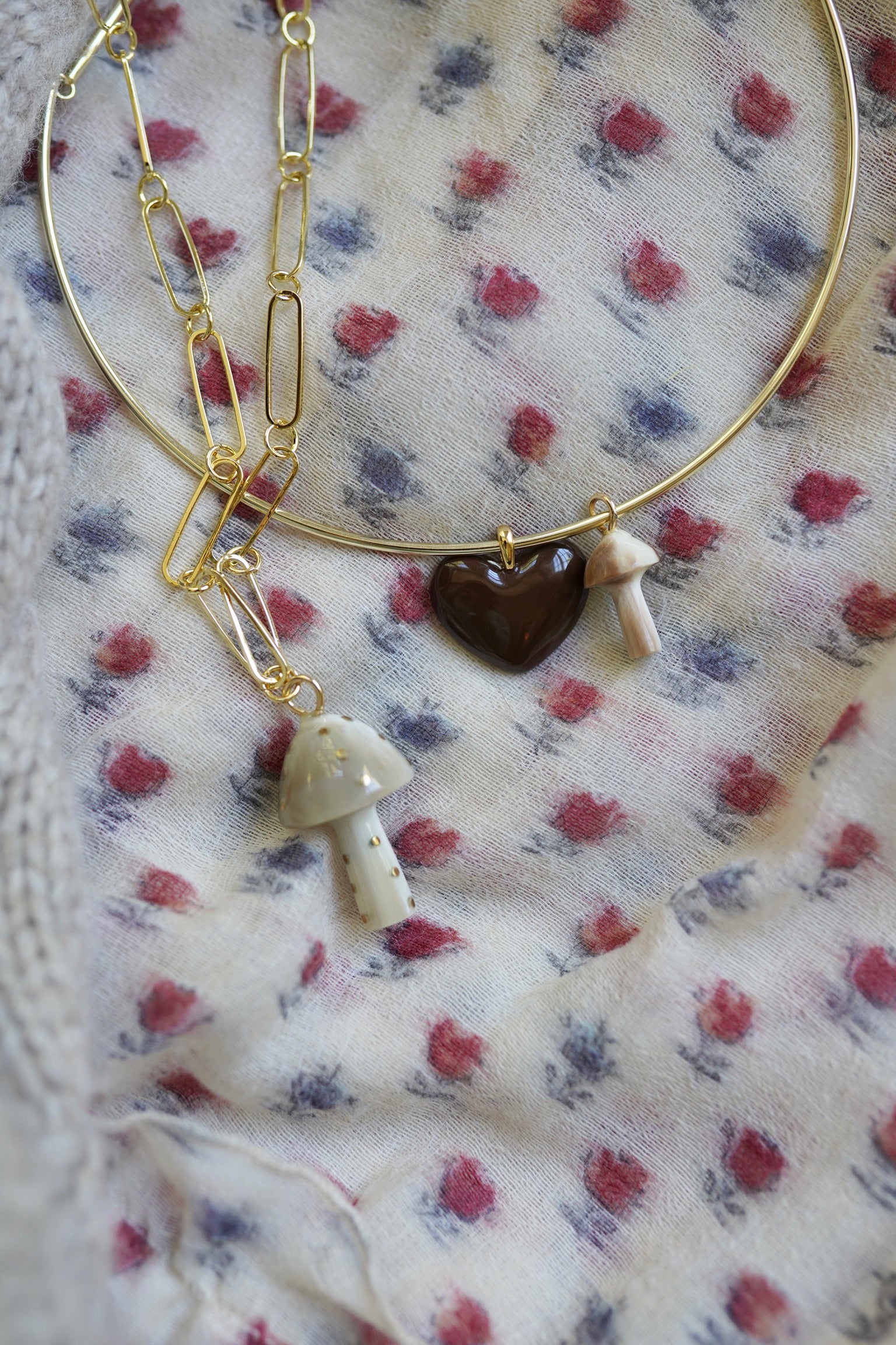 Gold necklace with heart and mushroom charms on a floral fabric background