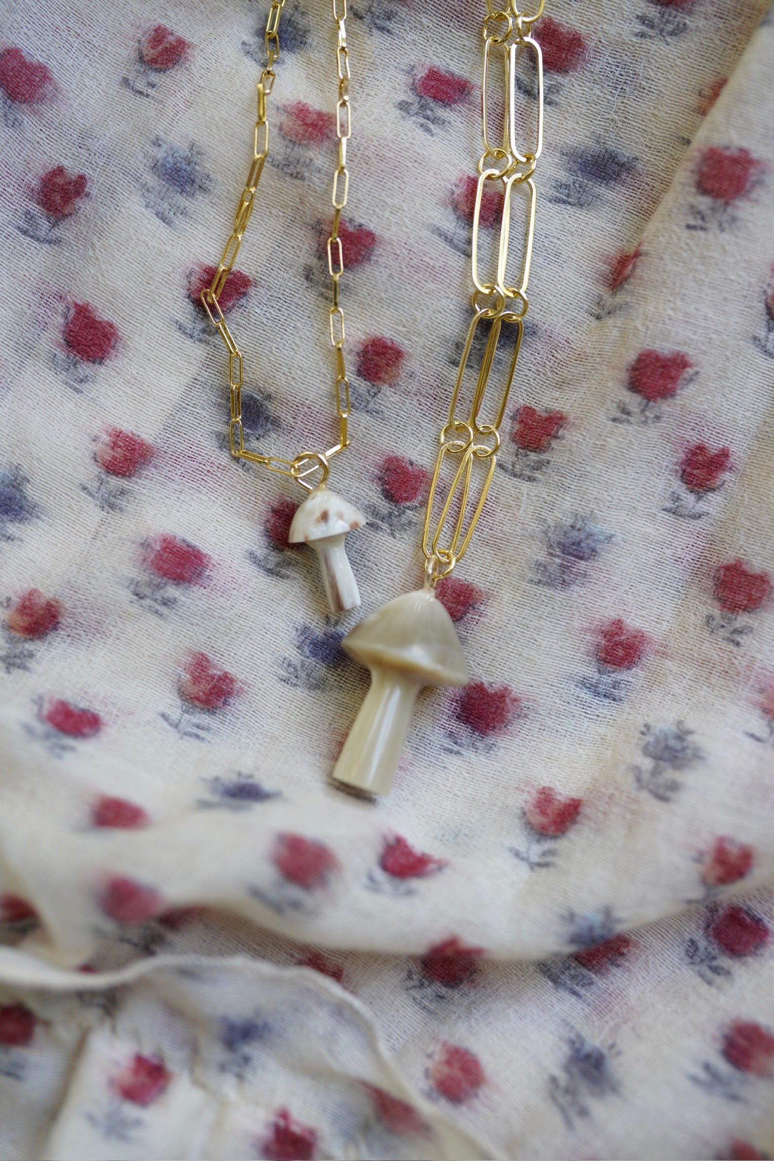 Gold necklace with mushroom pendants on a floral fabric background