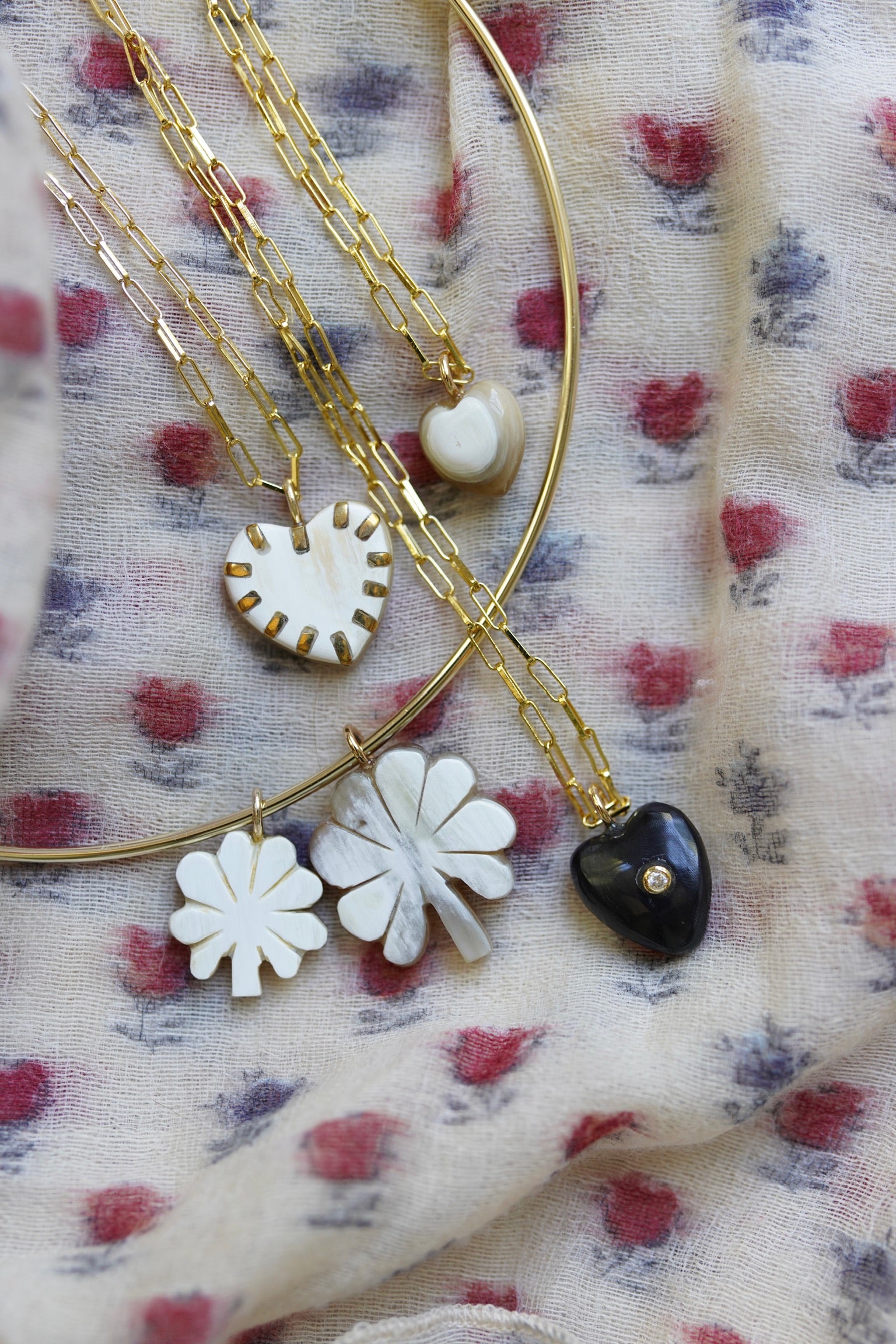 Gold necklaces with floral and heart charm pendants on a floral fabric background
