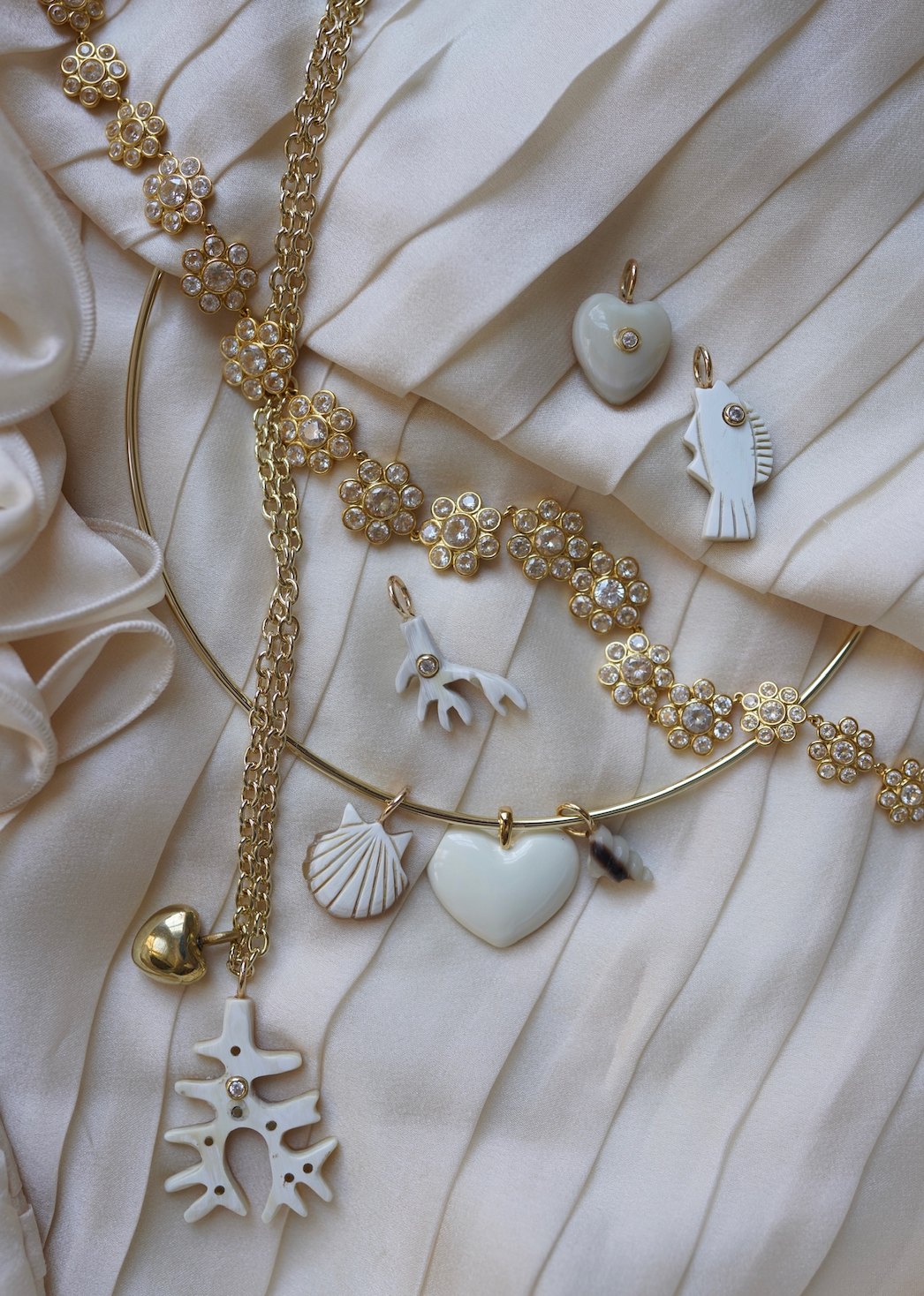 Gold jewelry with heart and shell charms on a textured beige fabric background